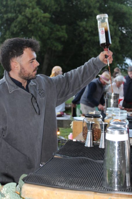 A man gracefully pours a drink from a tall glass at an outdoor event.