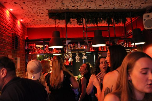 A lively bar scene with people socialising under warm red lighting.