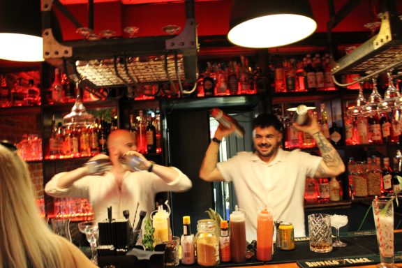 Two bartenders cheerfully mixing drinks at a vibrant, illuminated bar.
