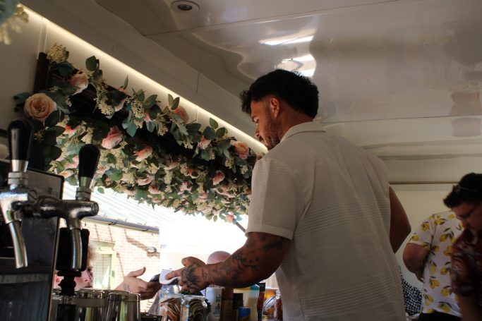 A bartender serves drinks in a floral-decorated bar area.